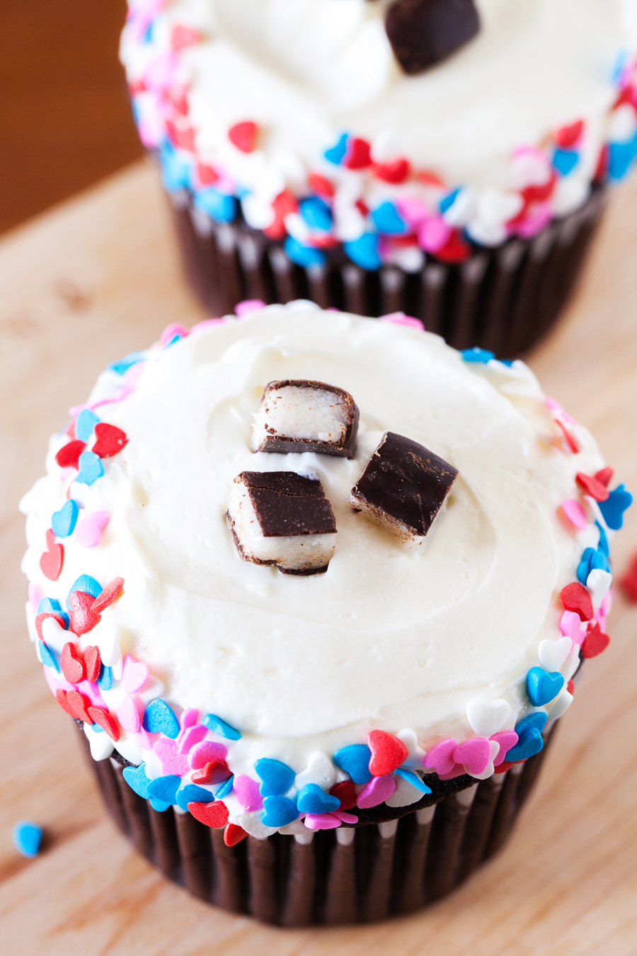 Close-up of two chocolate cupcakes with peppermint frosting and heart sprinkles.