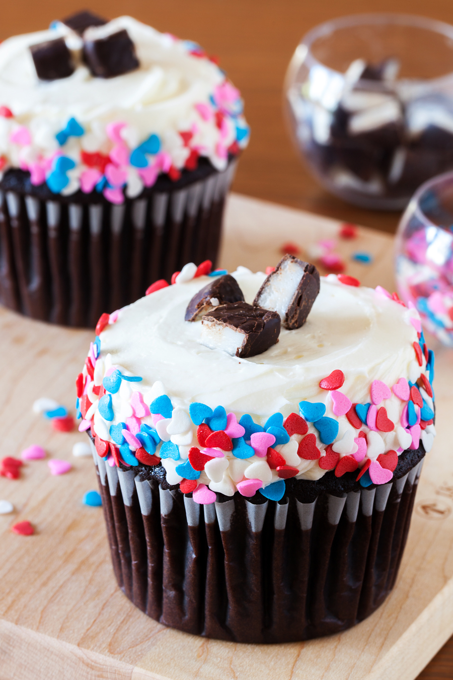 Two chocolate cupcakes with peppermint frosting and heart sprinkles.