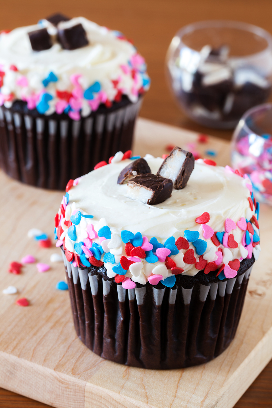 Two chocolate cupcakes with peppermint frosting and heart sprinkles.