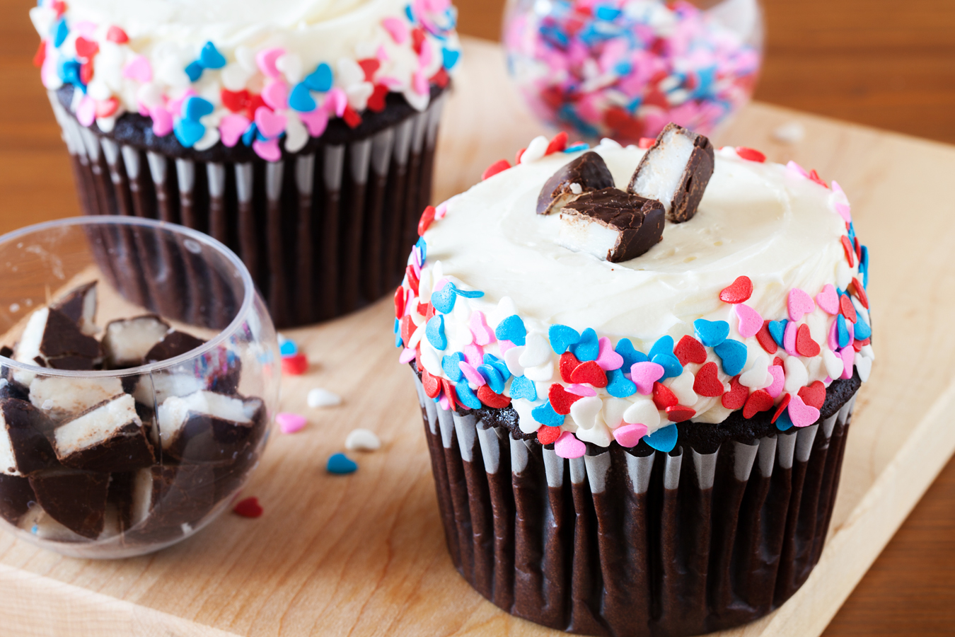 Horizontal image of two chocolate cupcakes with peppermint frosting and heart sprinkles.