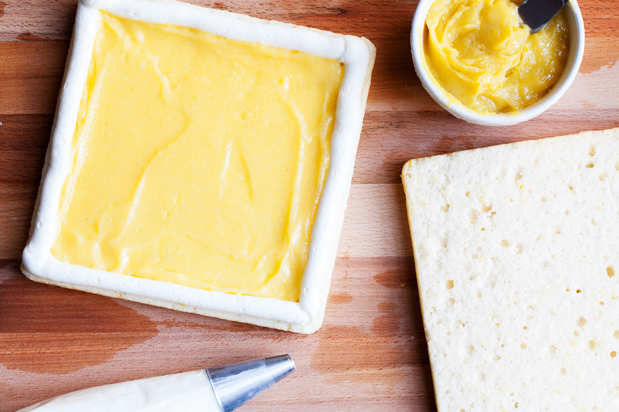 Two layers of soft white cake, lemon curd filling, and cream cheese frosting make this Lemon Snack Cake the perfect “light” and bright dessert.