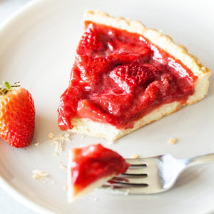 Slice of strawberry tart on a plate with fork. 