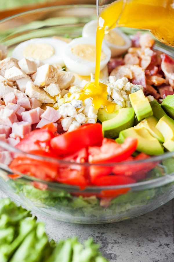 Dressing being poured in a bowl of cobb salad. 