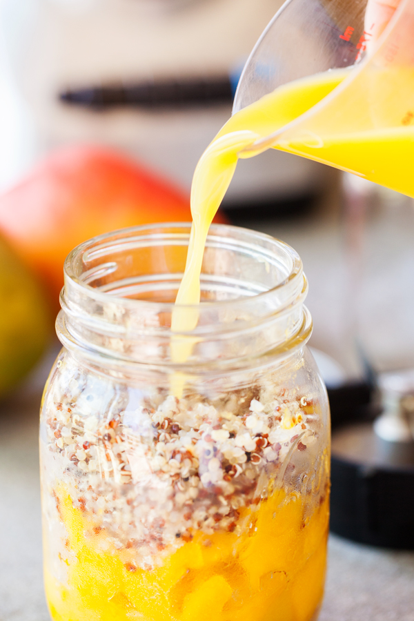 Juice being poured into mason jar of fresh mangoes and quinoa. 