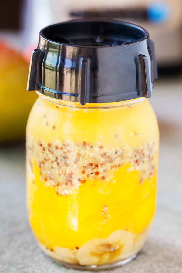 Mason jar with lid of bananas, mangoes, quinoa, and juice. 