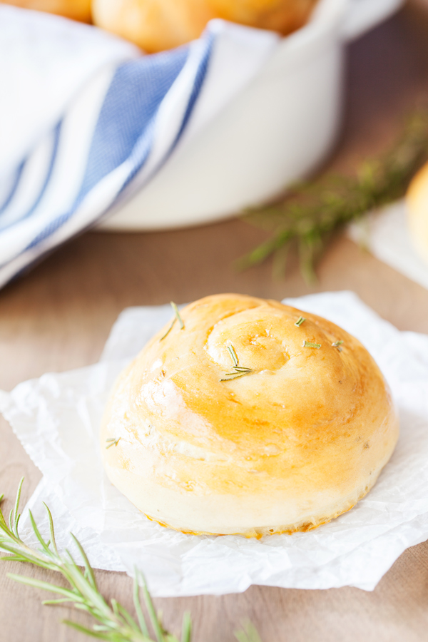 Rosemary Dinner Roll on parchment paper with bread basket in the background. 