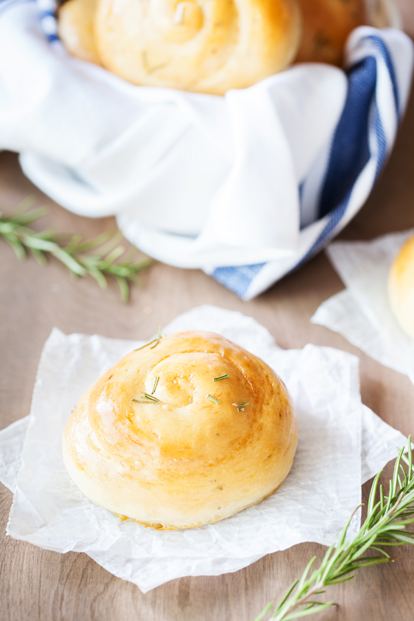 Rosemary Dinner Roll on parchment paper with bread basket in the background. 