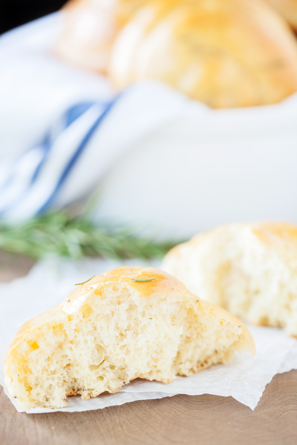 Split open Rosemary Dinner Roll on parchment paper and bread basket in the background. 