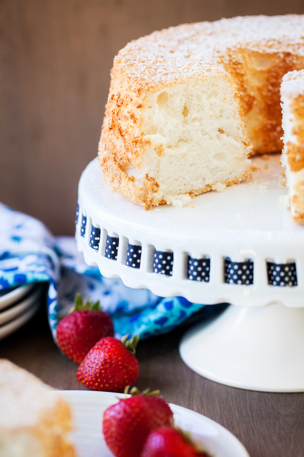 Angel food cake on a cake stand surrounded by fresh strawberries. 