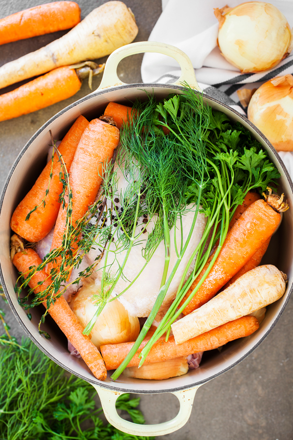 Raw chicken, carrots, onions, parsnips, peppercorn, dill, and parsley in a pot. 