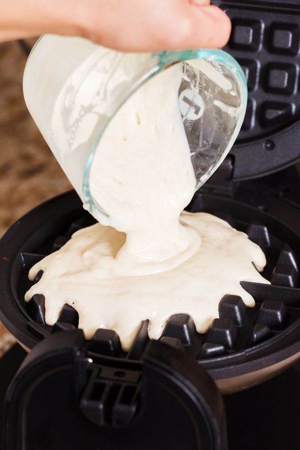 Yeast waffle batter being poured into waffle iron. 