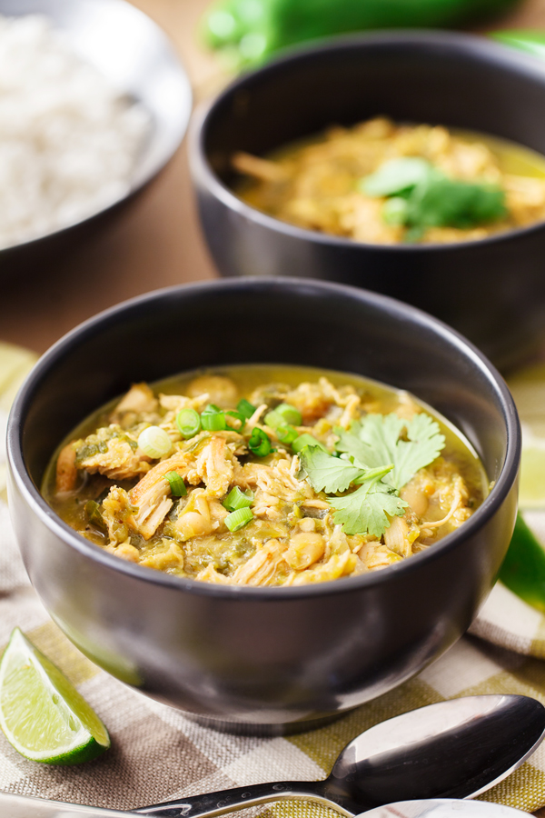 Two bowls of white chicken chili with rice in the background and lime wedge in the foreground. 