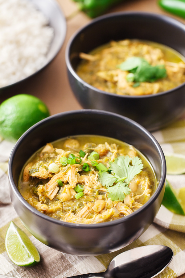 Two bowls of white chicken chili with rice in the background and lime wedge in the foreground. 