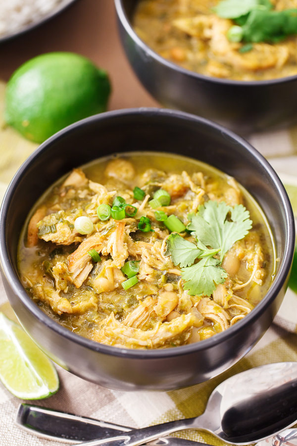 Two bowls of white chicken chili with rice in the background and lime wedge in the foreground. 