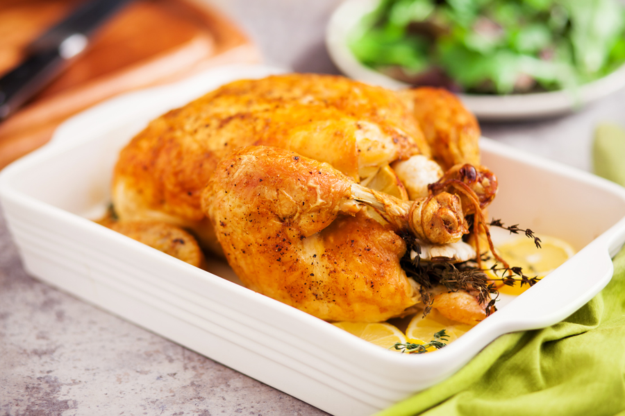 Roast chicken in a baking pan with lemon slices, springs of thyme, and a side salad in the background. 