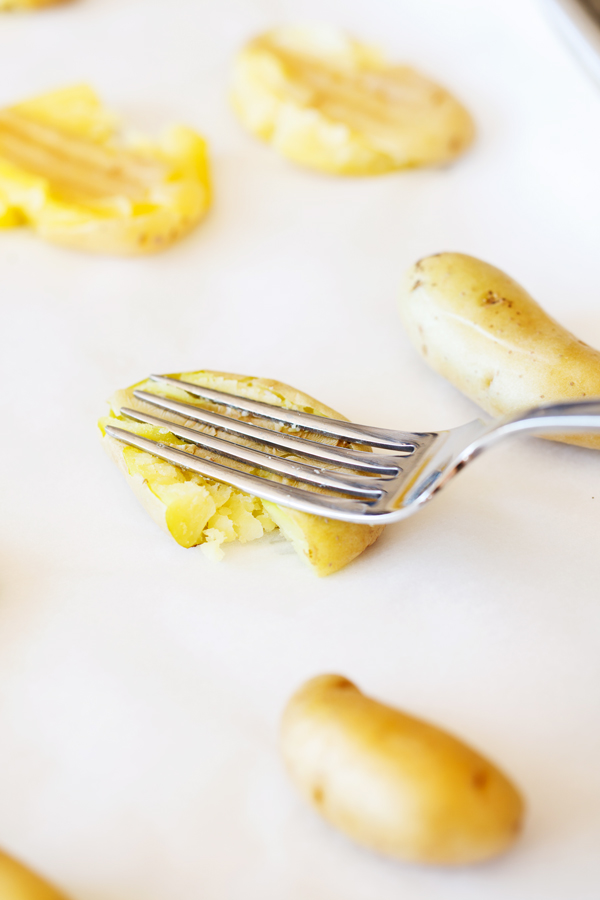 Baked fingerling potatoes on parchment paper being smashed with a fork. 