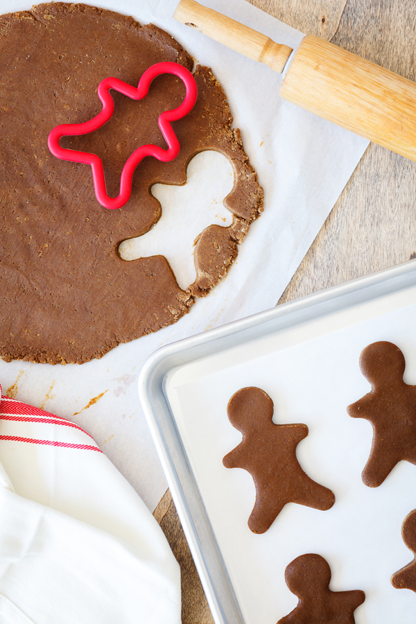 Birds-eye view of gingerbread cookie dough cut-outs on a baking sheet surrounded with a rolling pin and rolled out gingerbread cookie dough.
