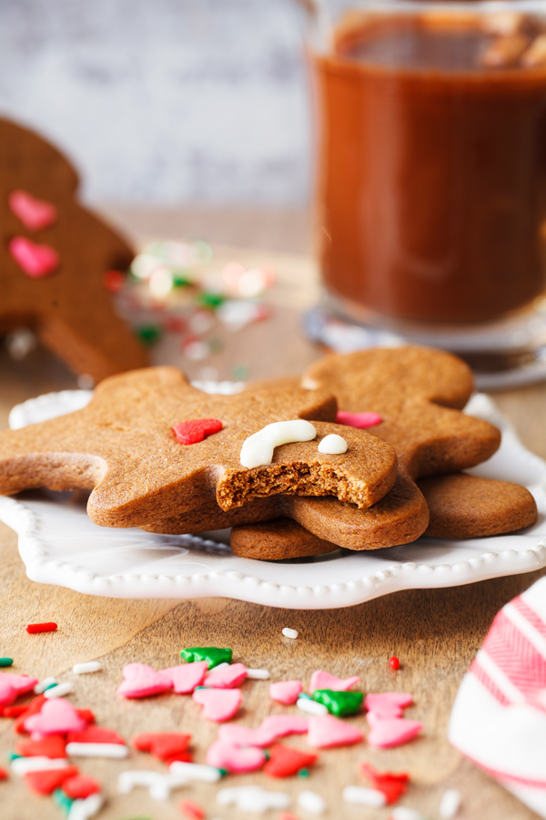 Partially bitten gingerbread cookie on a plate with a glass of hot chocolate in the background. 