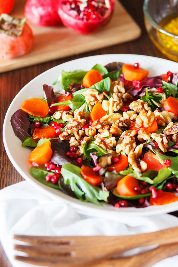 Persimmon and pomegranate salad with fresh pomegranate, persimmon, and dressing in the background.