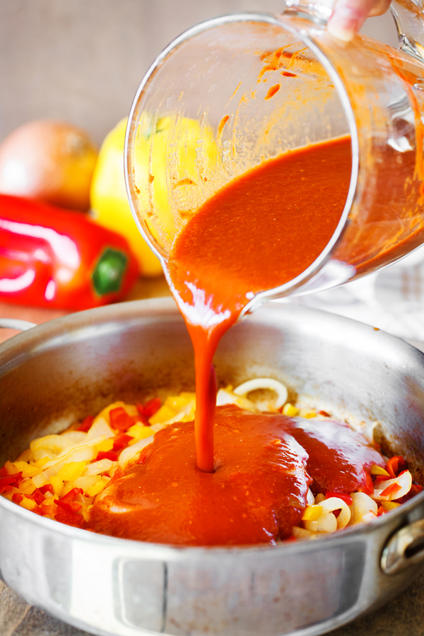 Red sauce being poured into a pan with fajita vegetables. 
