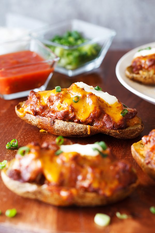 Chili Cheese Stuffed Potato Skins with salsa, scallions, and sour cream garnishes in the background. 