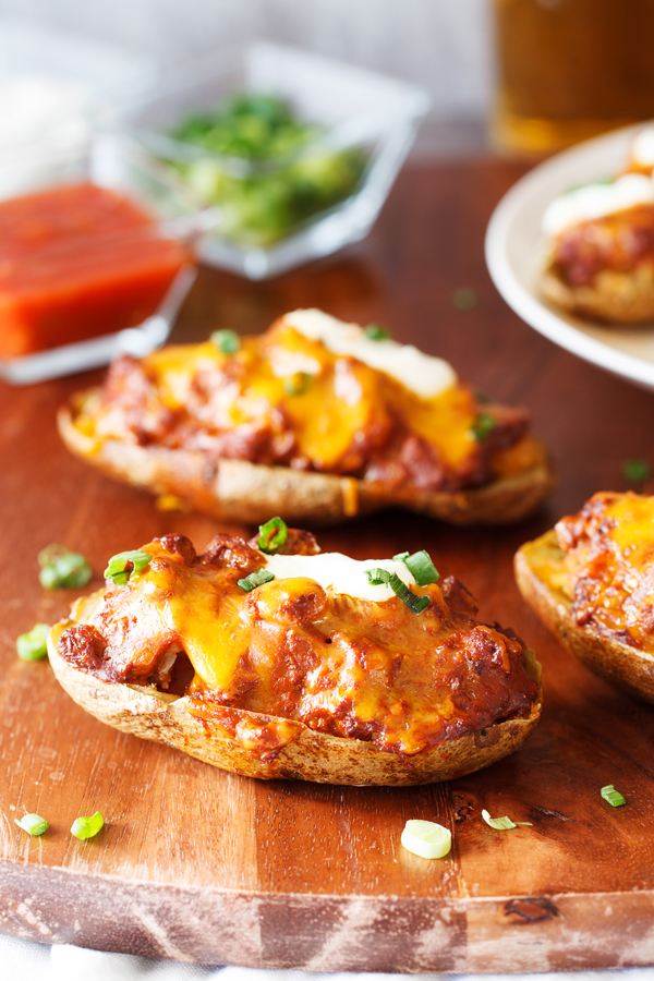 Chili Cheese Stuffed Potato Skins with salsa, scallions, and sour cream garnishes in the background. 