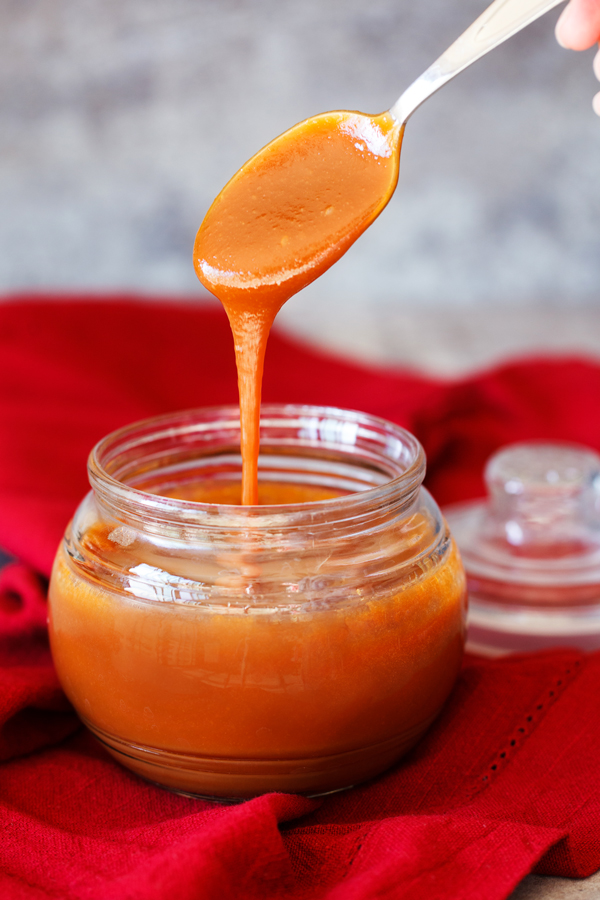 Spoon dipped in dulce de leche and pulled out over a jar.  