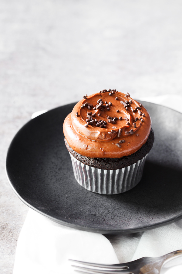 Chocolate cupcake frosted with chocolate frosting and chocolate sprinkles on a plate. 
