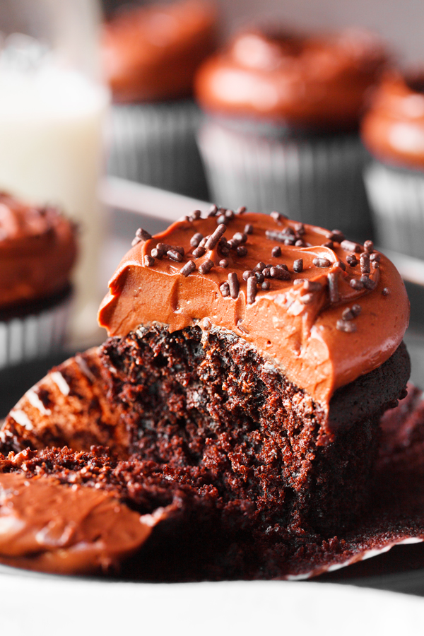 Partially eaten chocolate cupcake with chocolate frosting and liner peeled off. 