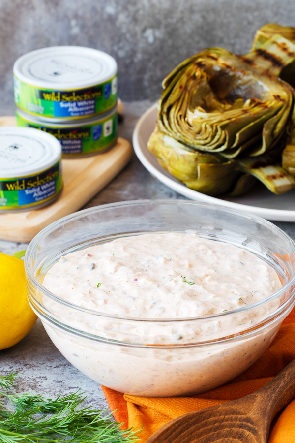 A bowl of tuna salad in the foreground with grilled artichokes in the background. 