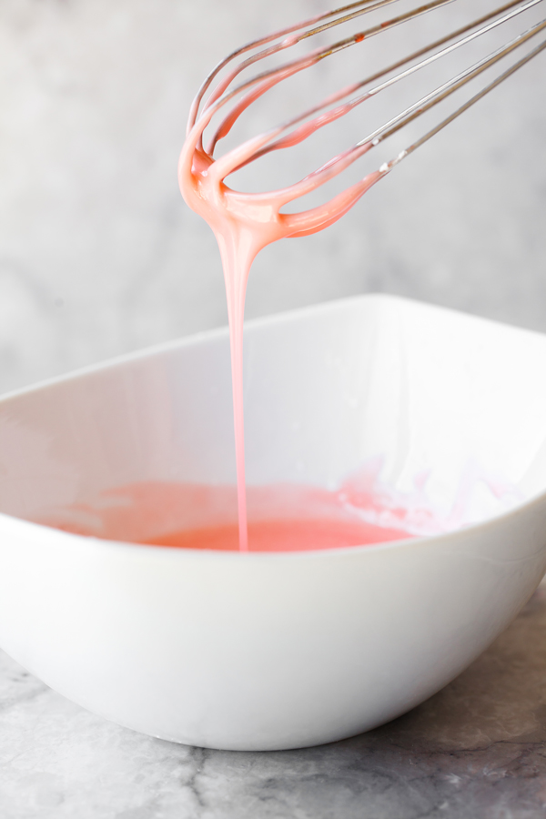 Stream of strawberry glaze dripping off a whisk into a bowl. 