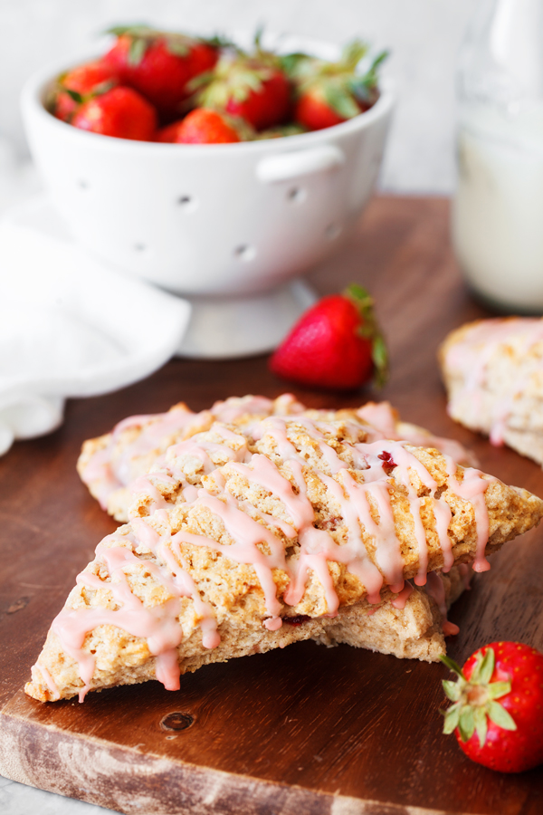 Two strawberry scones on a board with fresh strawberries in a colander in the background. 