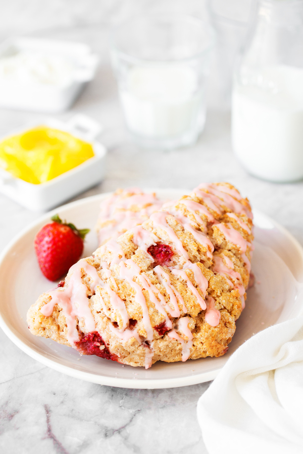 Strawberry scone on plate with lemon curd, butter, and milk in the background. 