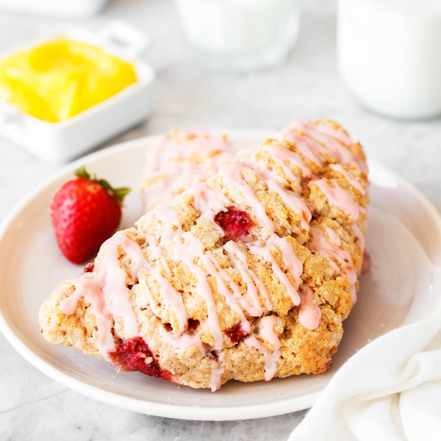 Strawberry scone on plate with lemon curd, butter, and milk in the background.