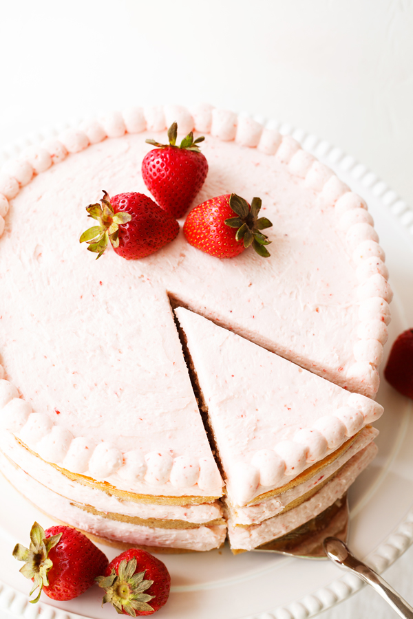 Slice of fresh strawberry cake being pulled out of whole cake.
