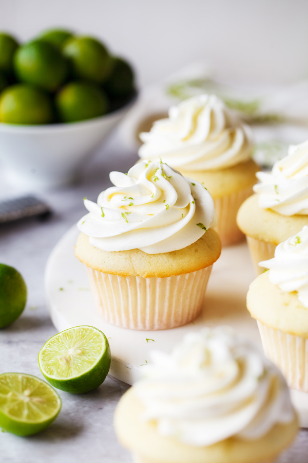 Key lime cupcakes topped with key lime buttercream, with fresh key limes in the foreground and background. 