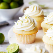 Key lime cupcakes topped with key lime buttercream, with fresh key limes in the foreground and background.