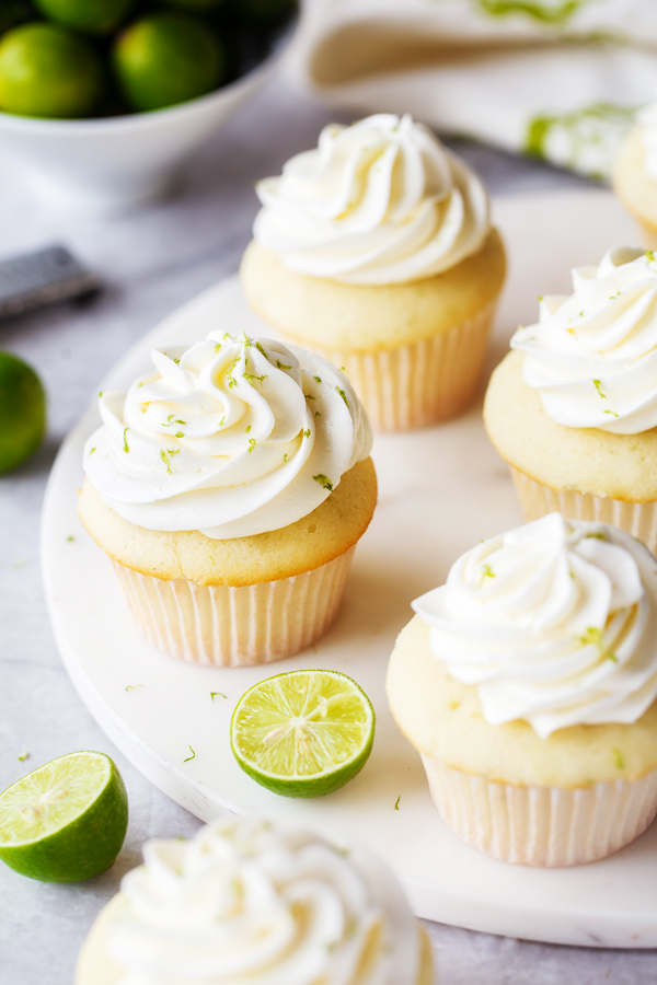 Key lime cupcakes topped with key lime buttercream, with fresh key limes in the foreground and background. 