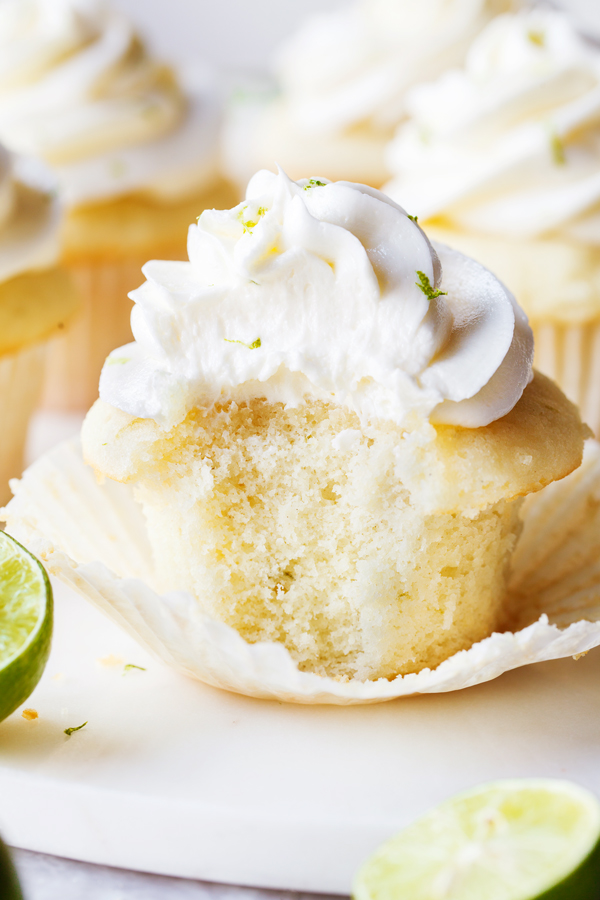 Bitten key lime cupcake topped with key lime buttercream with cupcake liner peeled off.