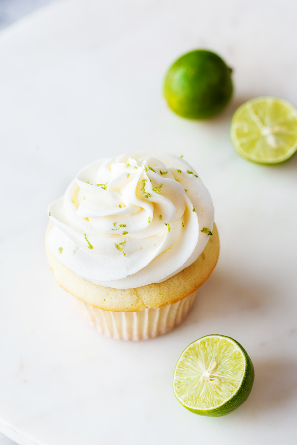 Single key lime cupcake topped with key lime buttercream, with fresh key limes in the foreground and background. 