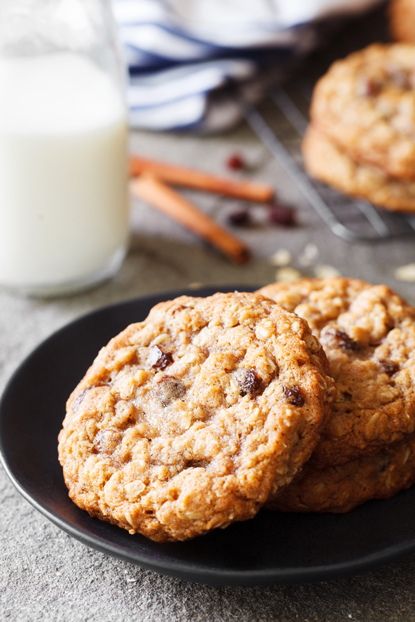 Thick and chewy oatmeal raisin cookies on a plate with milk in the background.