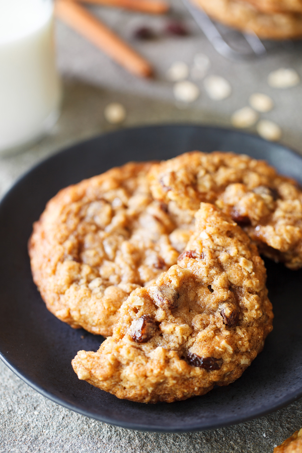 Half eaten thick and chewy oatmeal raisin cookie on a black plate.