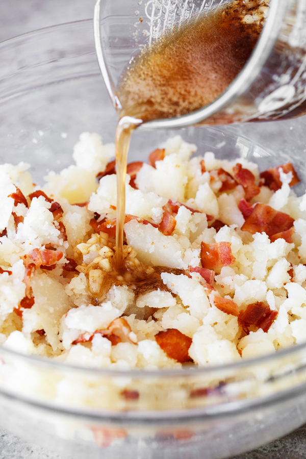 Preparation step for Cheesy Bacon Garlic Stuffed Potato Skins - Bacon grease poured into bowl with potatoes, bacon, and garlic