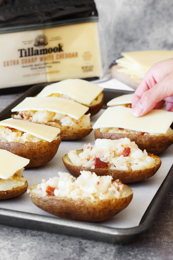 Preparation step for Cheesy Bacon Garlic Stuffed Potato Skins - Slice of Tillamook's Extra Sharp White Cheddar being placed on stuffed potato skins