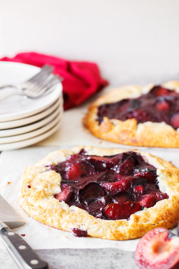 Plum crostata on parchment paper with plates and utensils in the background. 