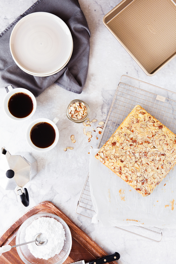 Overhead view of Swedish Visiting Cake Bars with cups of coffee, serving plates, powdered sugar, and sliced almonds.