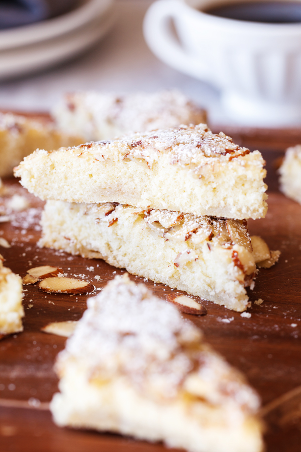 Stack of Swedish visiting cake bars on a board with a cup of coffee and plates in the background. 