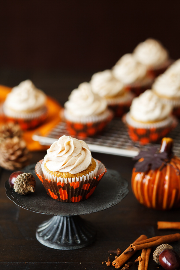 Pumpkin spice cupcake with cinnamon cream cheese frosting on cake pedestal.