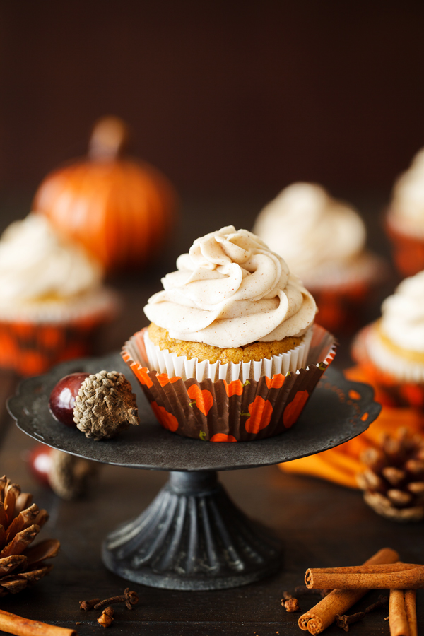 Pumpkin spice cupcake with cinnamon cream cheese frosting on cake pedestal.