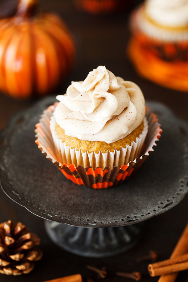 Pumpkin spice cupcake with cinnamon cream cheese frosting on cake pedestal.